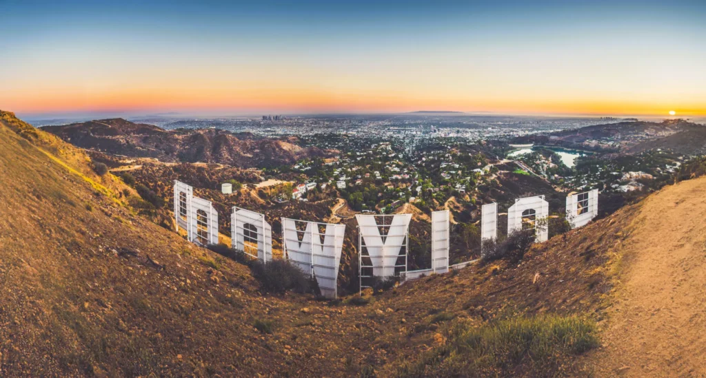 View of the Hollywood sign from behind, overlooking the cityscape of Los Angeles at sunset.