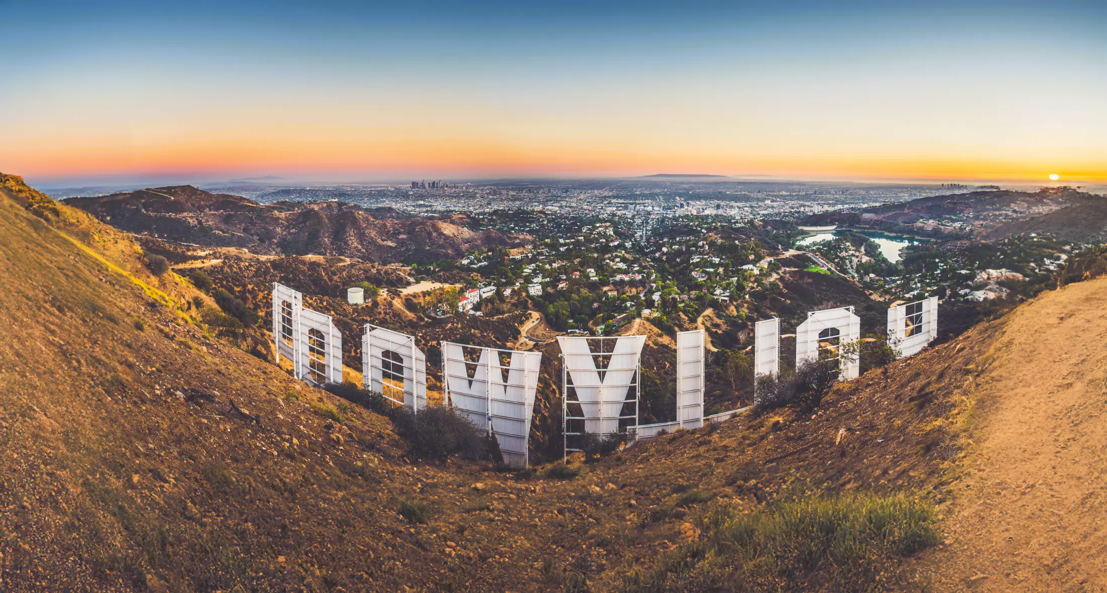 View of the Hollywood sign from behind, overlooking the cityscape of Los Angeles at sunset.