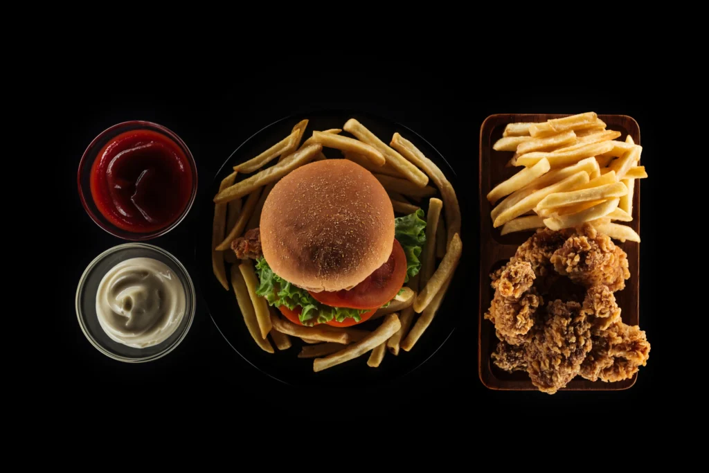 Top view of a meal consisting of a burger with fries, fried chicken, and dipping sauces on a black background.